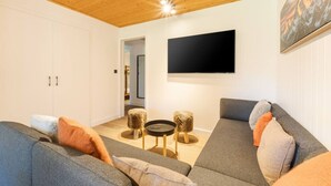 Moderni olohuone, jossa on puinen katto, seinälle asennettu taulutelevisio ja sohvaryhmä koristetyynyineen.