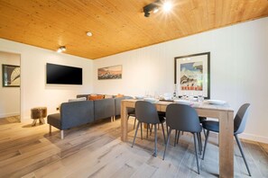 A modern living room with a wooden ceiling, a grey sofa, a dining table with chairs, and artwork on the walls. - Géroux- Modern Apt | Quiet | Mountain View | Garden (Chamonix-Mont-Blanc)
