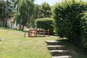 A garden with a table and chairs, a stone pathway, and a hedge. - Géroux- Modern Apt | Quiet | Mountain View | Garden (Chamonix-Mont-Blanc)