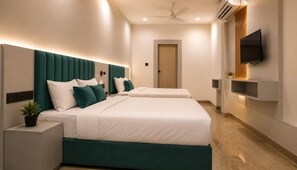 A hotel room with two beds, a flat-screen TV mounted on the wall, a ceiling fan, and an air conditioning unit. - hotel venue (Ahmedabad)