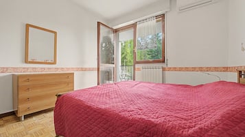 A bedroom with a bed, a wooden dresser, a mirror, and a window with a view of trees.