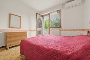 Un dormitorio con cama, cómoda de madera, espejo y ventana con vistas a árboles.