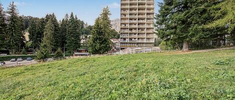 Un immeuble à plusieurs étages doté de balcons, entouré d’arbres et bordé d’un champ d’herbe.