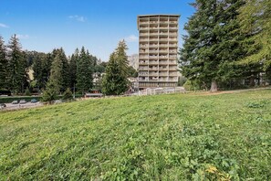 Un edifici de diverses plantes amb balcons, envoltat d'arbres i un camp de gespa.
