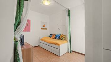 A bedroom with a bed, a desk, and a wall-mounted shelf.