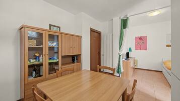 A dining area with a wooden table and chairs, a cabinet with glass doors, a door, a radiator, a green curtain, and a wall with a framed picture.