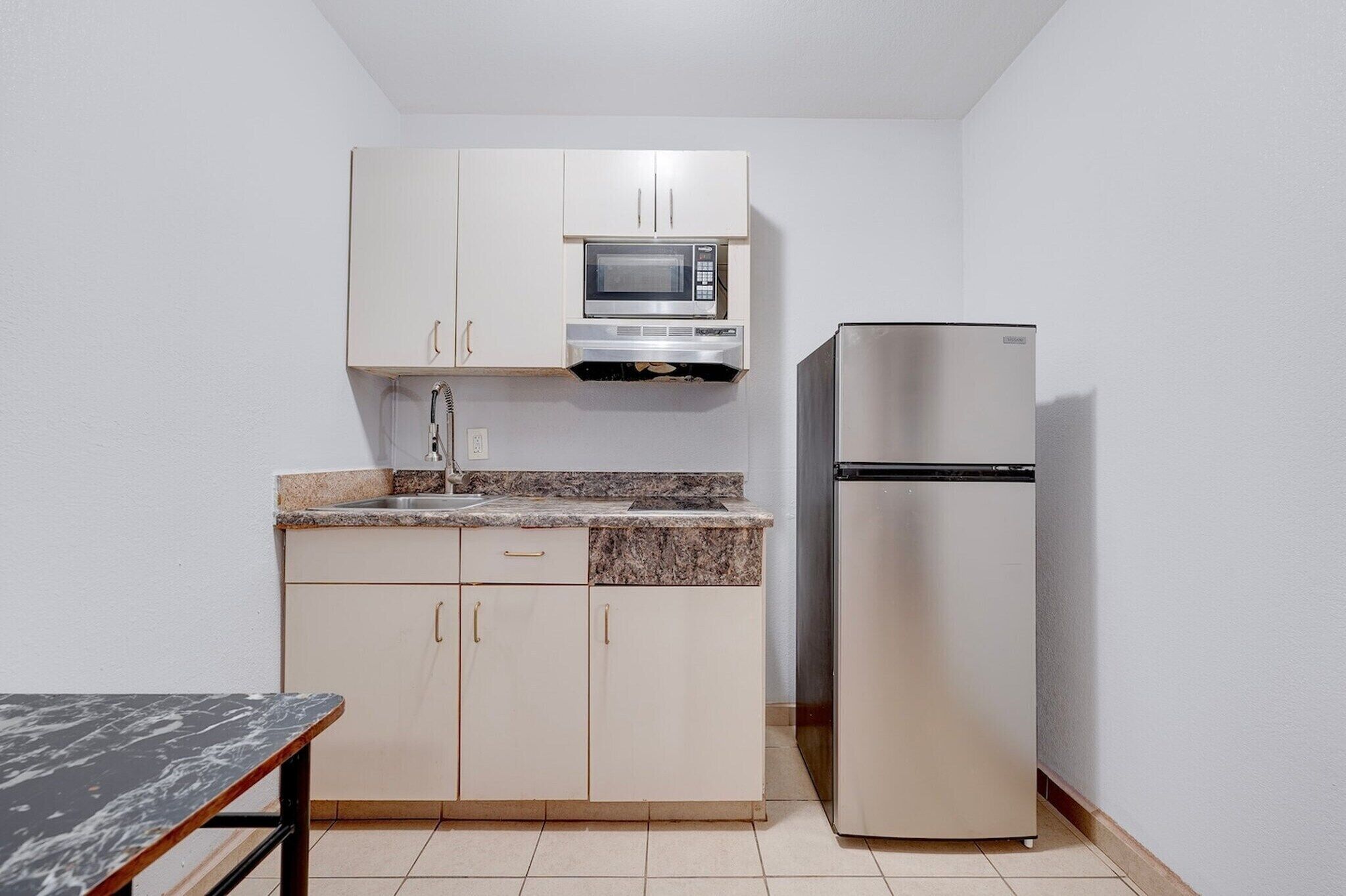 A compact kitchen with a microwave, a refrigerator, and a granite countertop.