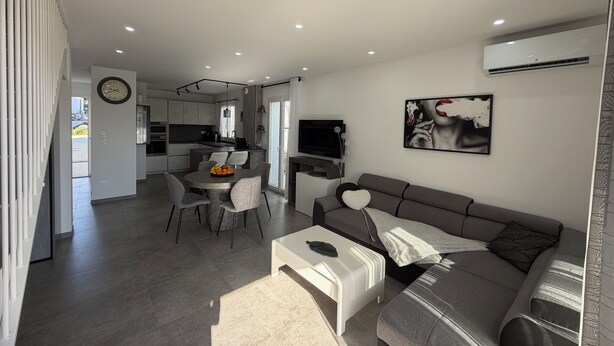 A modern living room with a grey sofa, a coffee table, and a dining area with a table and chairs. - Small, modern house with a garden, 3 km from the ocean (Aléria)