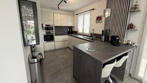 A modern kitchen with stainless steel appliances, a central island, and a view of the outdoors. - Small, modern house with a garden, 3 km from the ocean (Aléria)
