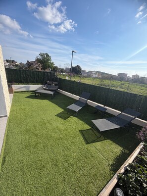 Ein Dachgarten mit Kunstgrasanlage, Sitzbereichen und Blick auf die Stadtlandschaft.