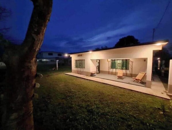 A modern house with a covered patio, two windows, and a lawn.