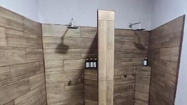 Ducha en esquina con paneles de madera y una columna central, suelo de baldosas y dos duchas empotradas en la pared.