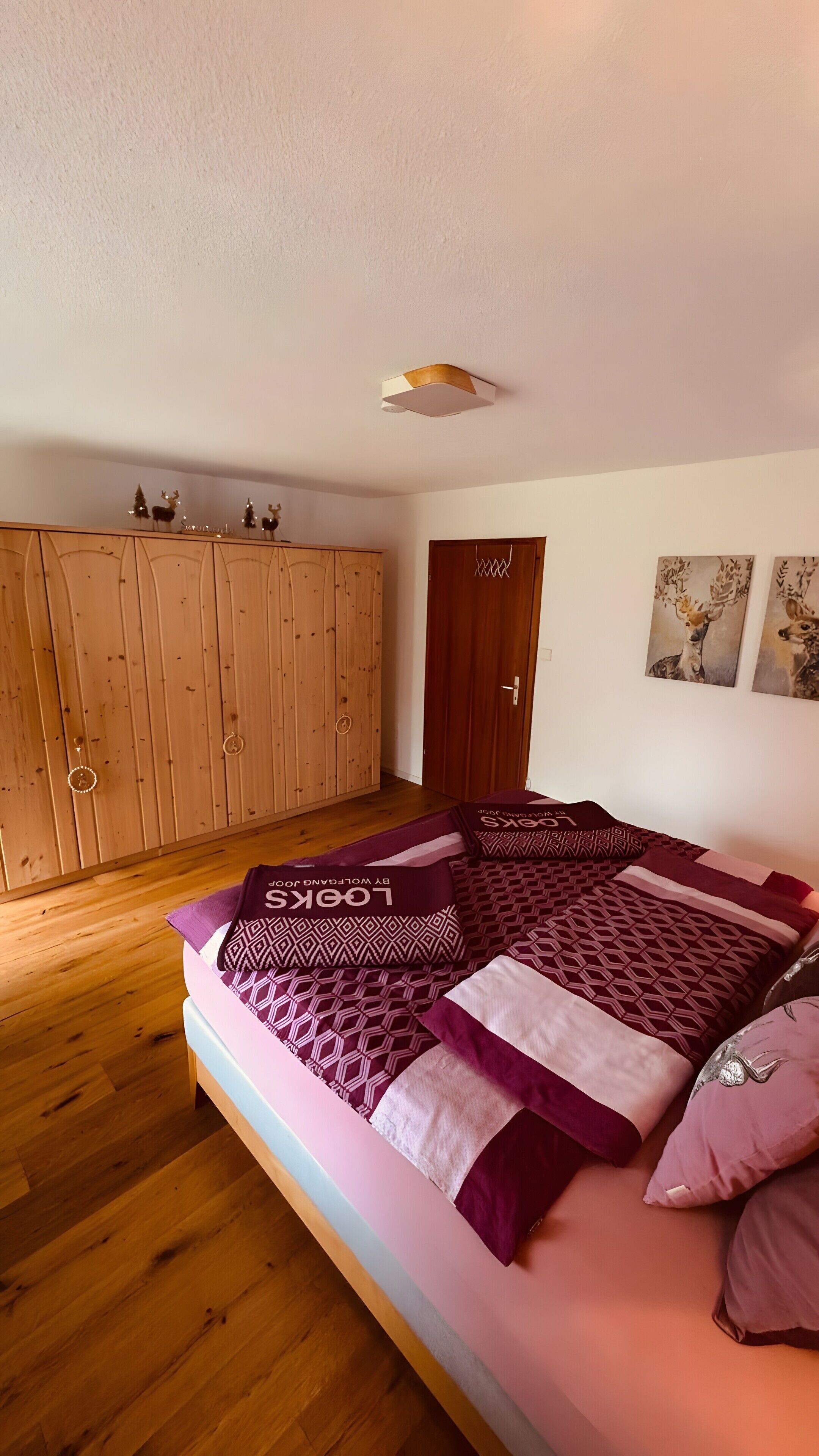 Un dormitorio con un armario de madera, una cama con ropa de cama estampada y dos cuadros colgados en la pared.