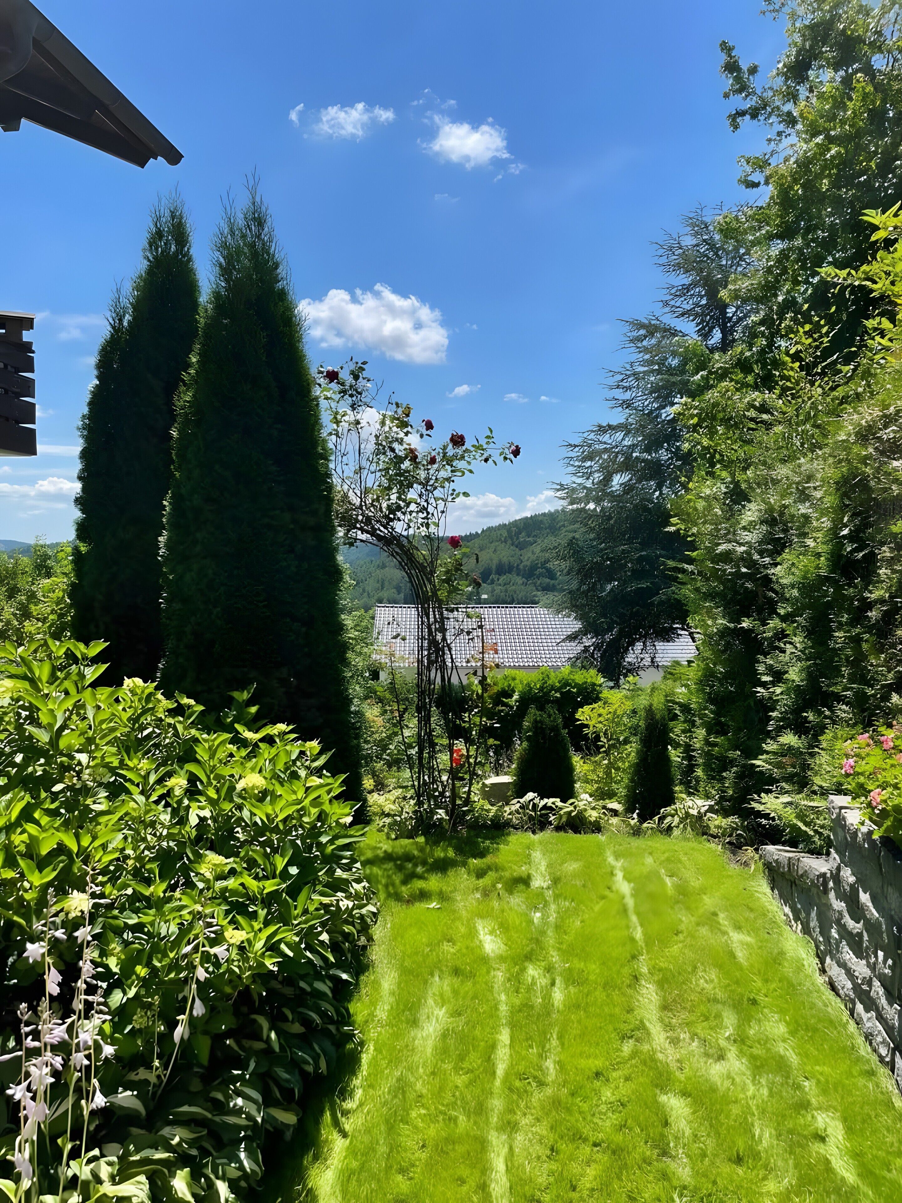 Un jardin bien entretenu, avec une pelouse, divers arbustes et un mur en pierre.