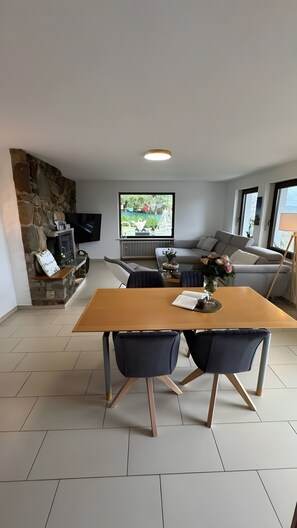 Una sala de estar moderna con chimenea de piedra, una mesa de comedor con sillas, un sofá y un televisor montado en la pared.