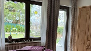 Un dormitorio con cama, ventana con cortinas, radiador y puerta.