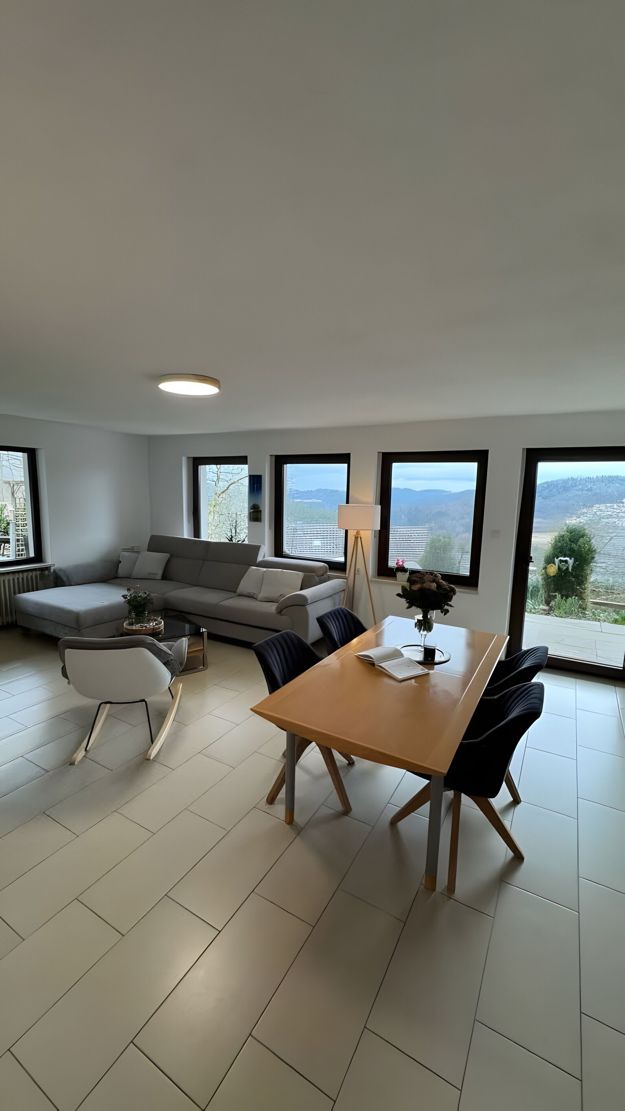 Un salon moderne comprenant un canapé, une table à manger avec des chaises et de grandes fenêtres donnant sur l’extérieur.