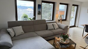 Una sala de estar moderna con un sofá seccional, una mesa de centro y ventanas grandes que ofrecen vistas a un paisaje nevado.