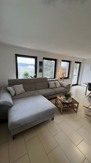 A modern living room with a sectional sofa, a coffee table, and large windows offering a view of a snowy landscape. - 5-Star Holiday Apartment Fernblick in the Bavarian Forest – 110 m² with Fenced Garden (Thurmansbang)