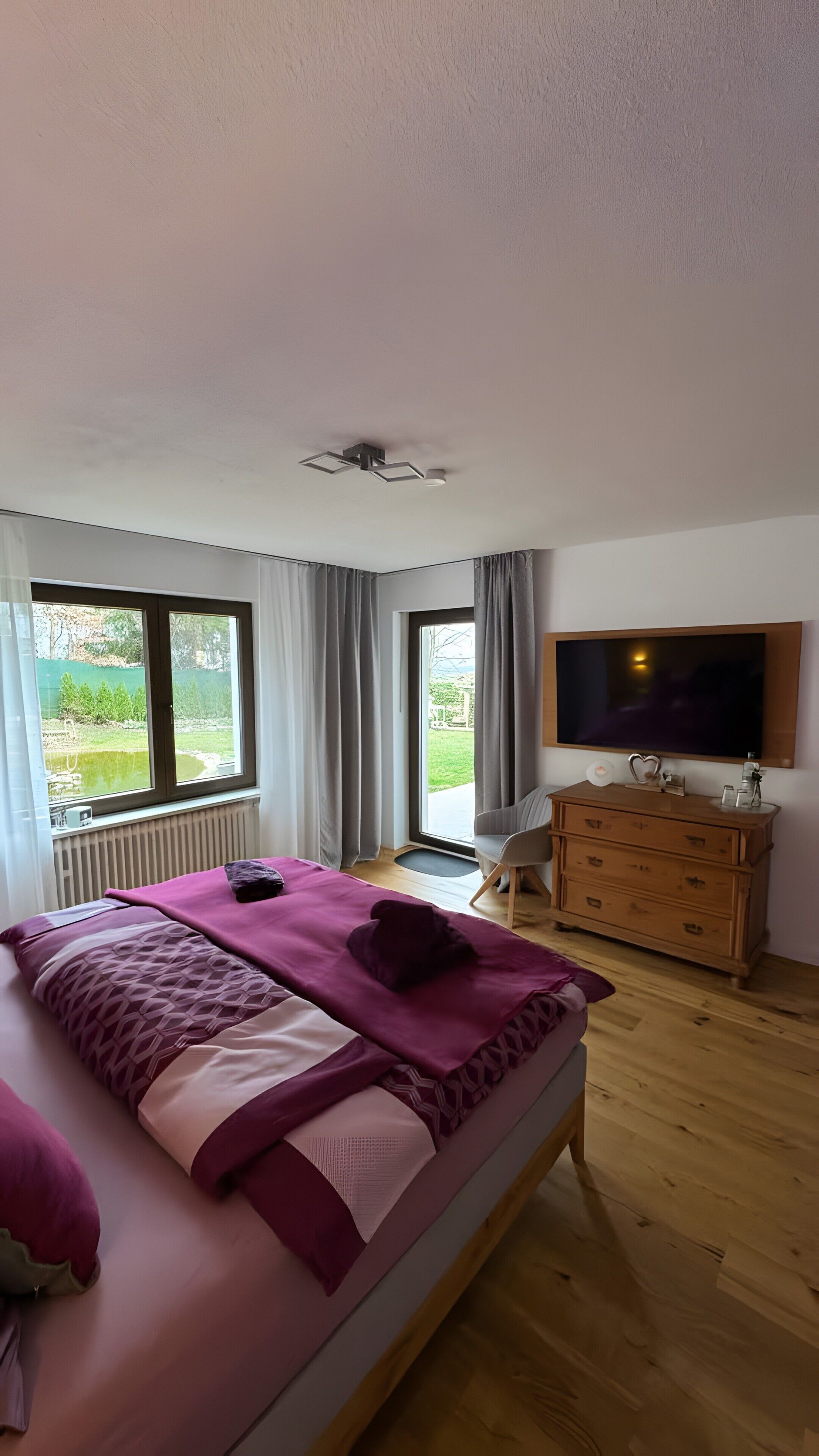 Ein Schlafzimmer mit einem Bett, einem Schminktisch, einem Fernseher und einem Fenster mit Vorhängen.