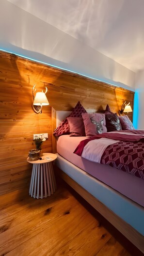Un dormitorio con cabecera de madera, una mesita de noche redonda y una cama con ropa de cama estampada.