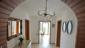 Un pasillo amplio con suelo de baldosas, un arco de entrada, una araña y un comedor al fondo.
