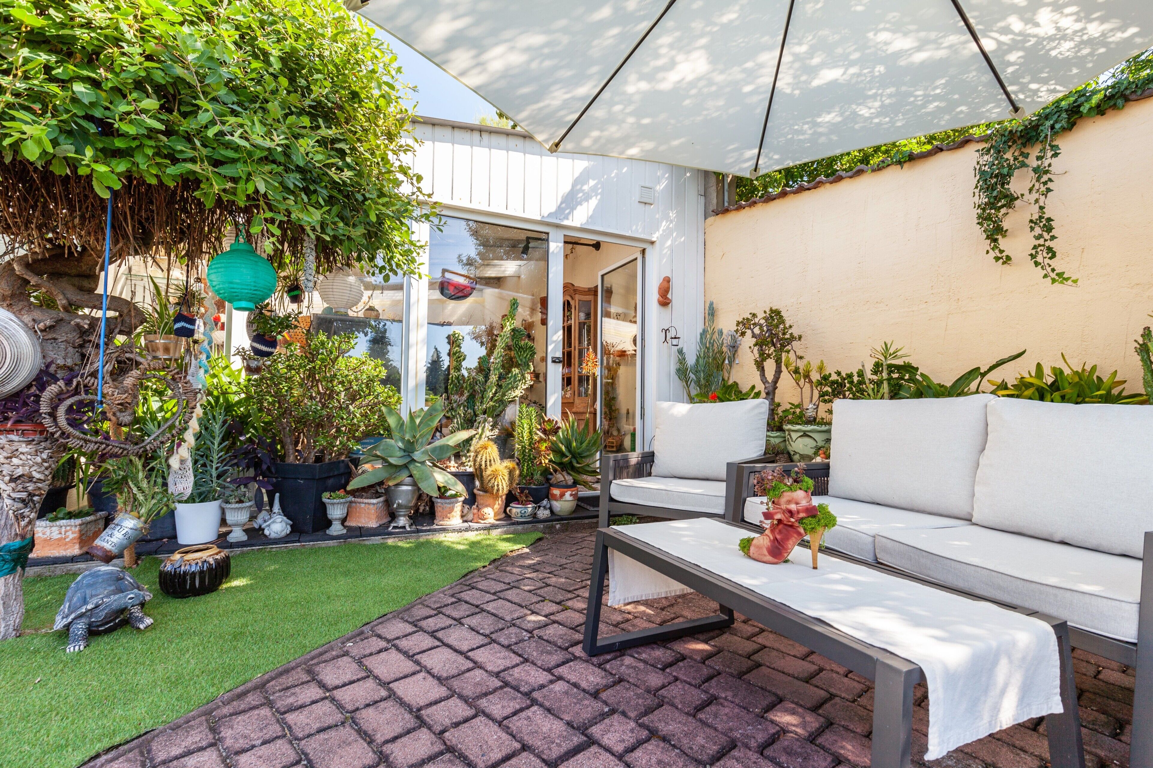 A patio area with a white sofa, a small table, and various potted plants.
