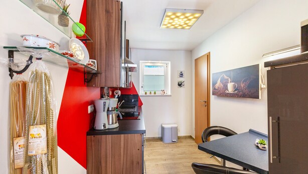 Una cocina funcional con cafetera, un cubo de basura y un comedor con una silla.