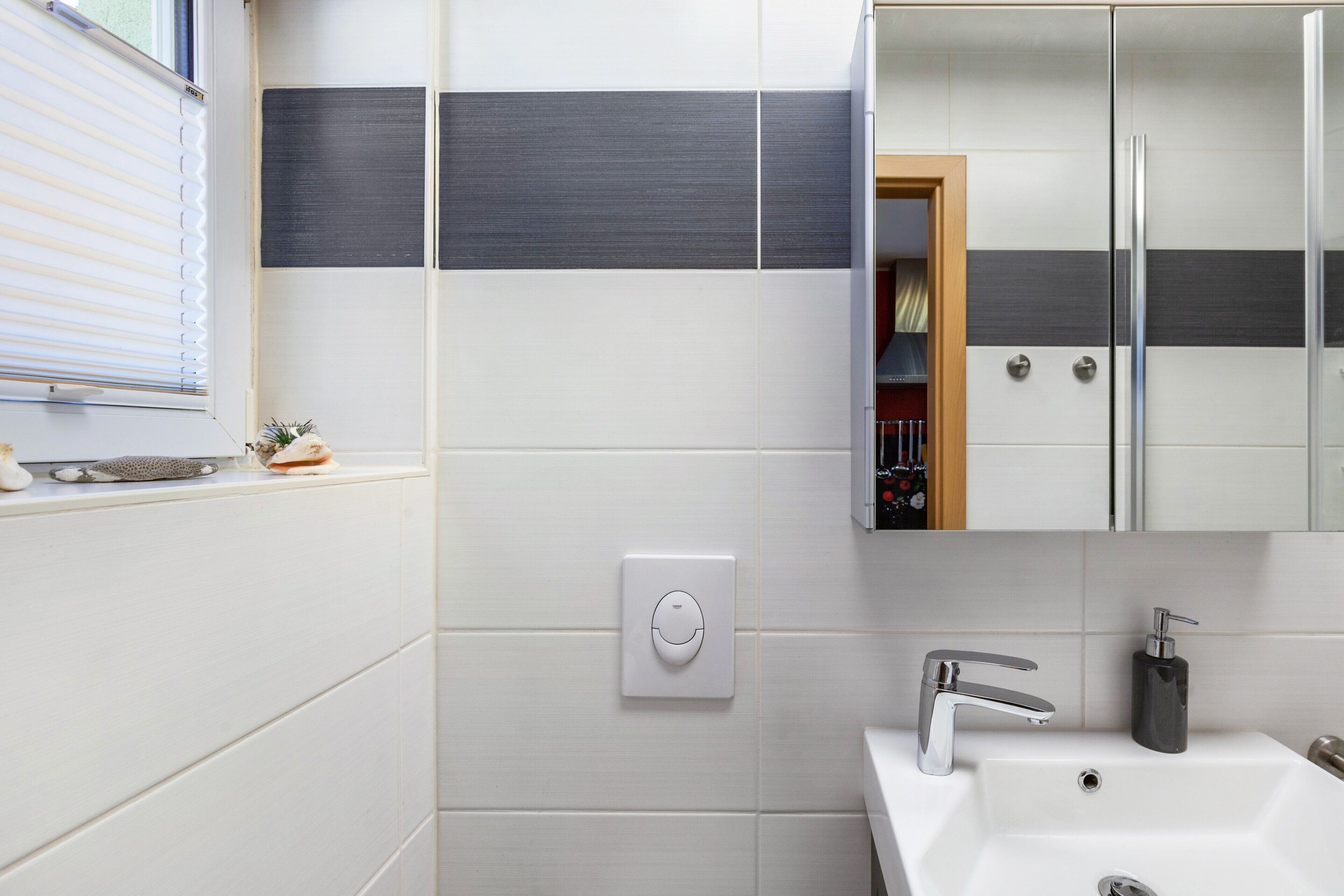 Un baño moderno con un lavamanos blanco, un espejo y una ventana con persianas.