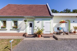 A two-story building with a white facade, a green door, and a small porch with two striped chairs.
