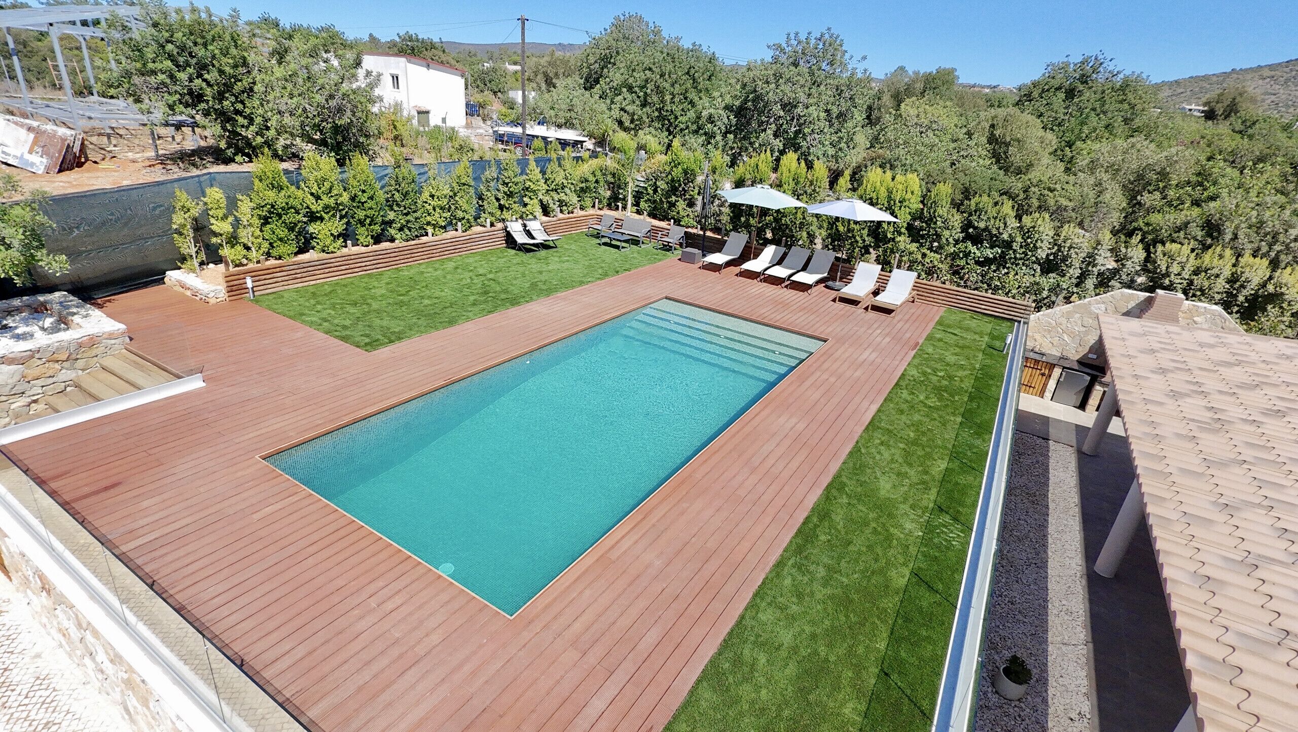 Ein rechteckiger Swimmingpool mit Holzdeck, einer Rasenfläche und einigen Liegestühlen.