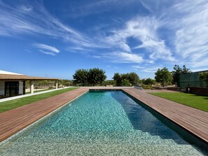 A rectangular swimming pool with clear water, surrounded by a wooden deck and a grassy area. - Algarve Country Modern Villa by Homing (Faro)