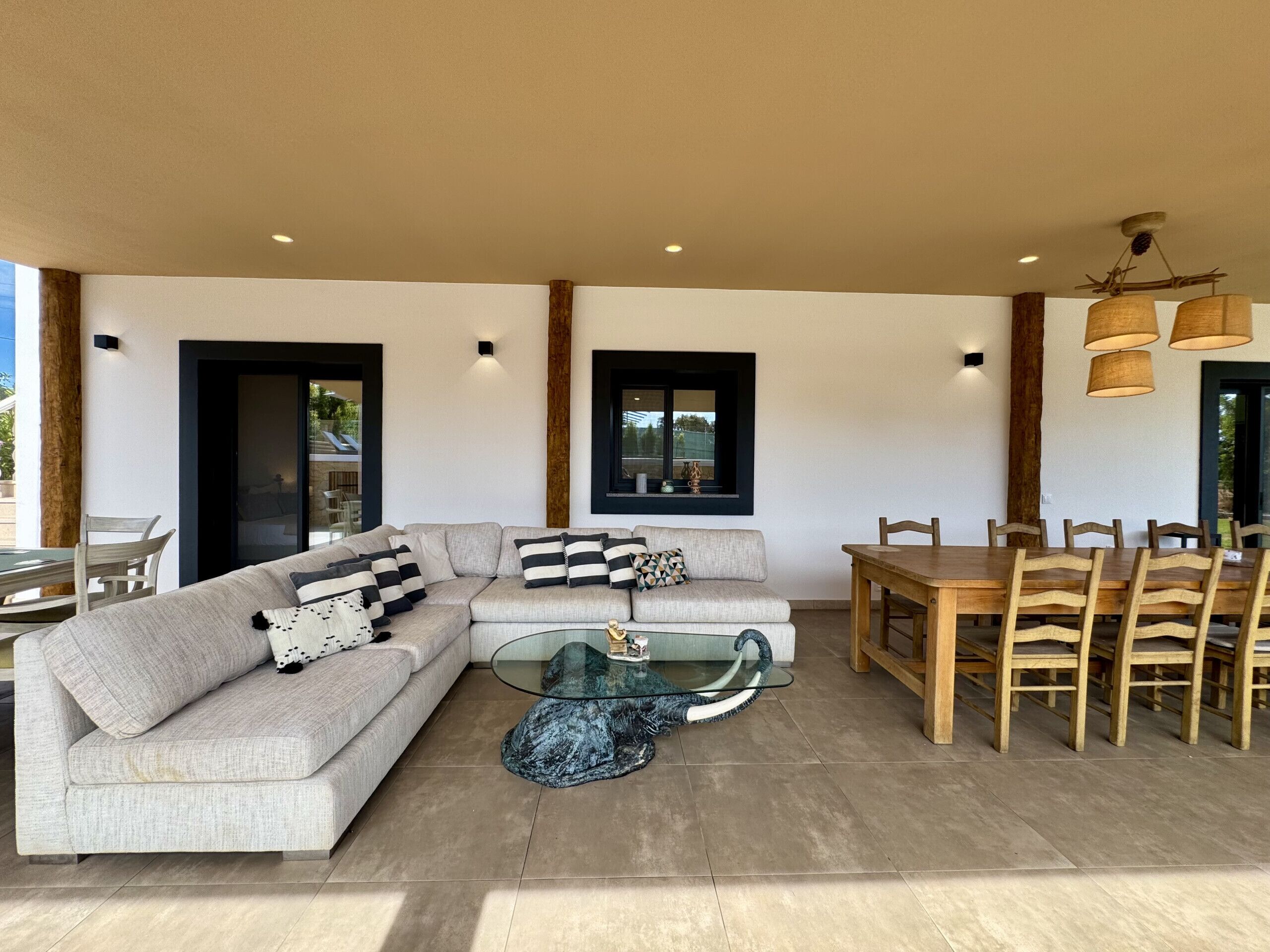 A modern living area with a sectional sofa, a glass coffee table, a dining table with chairs, and pendant lighting.