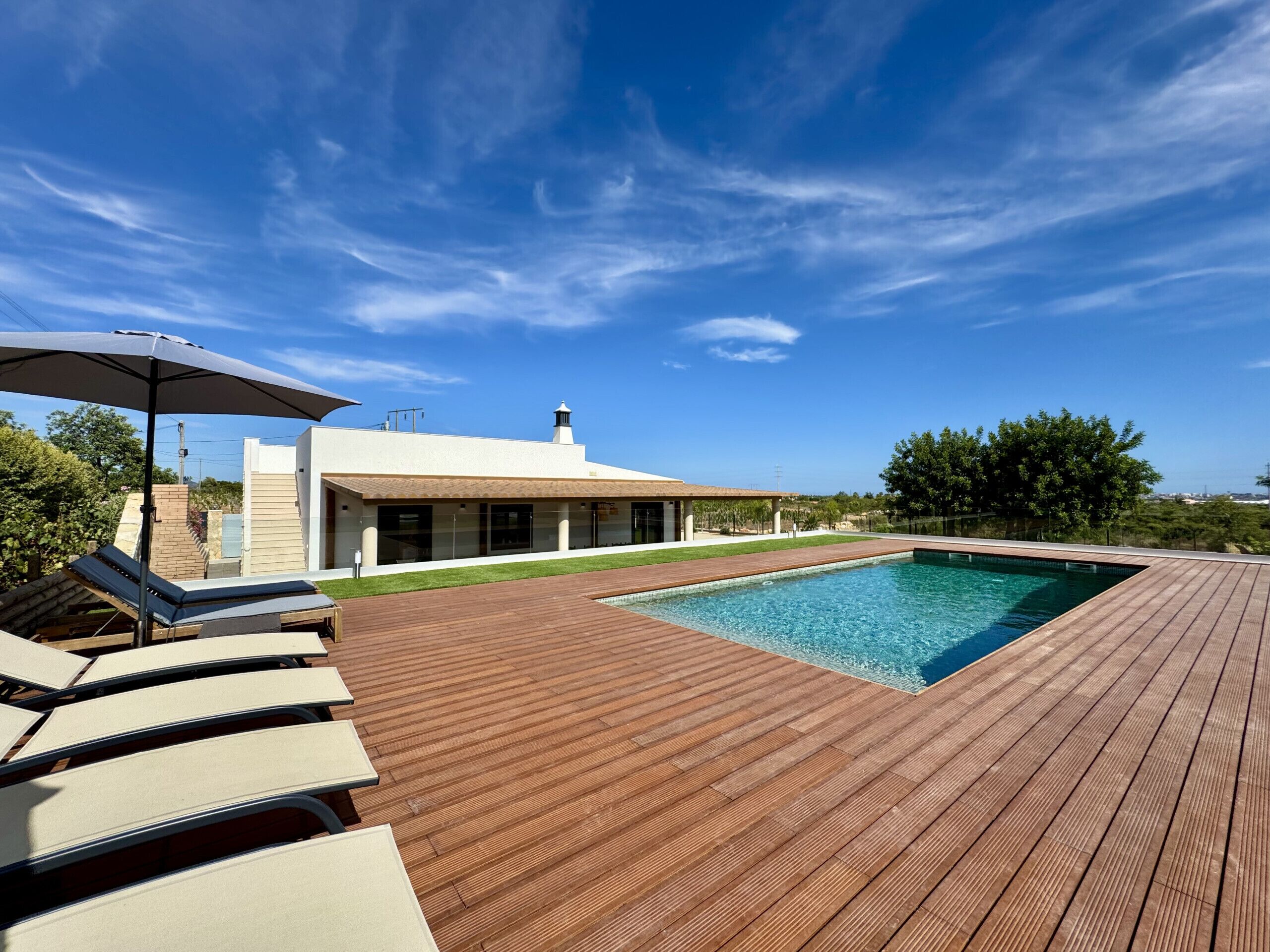 A swimming pool with a wooden deck, lounge chairs, and a building with large windows.