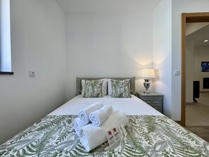 Ein ordentlich bezogenes Bett mit aufgerollten Handtüchern, einer Nachttischlampe und einer blumengemusterten Bettdecke.