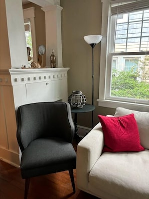 A room with a white fireplace, a black chair, a white sofa with a red pillow, and a floor lamp. - • Family Beach Condo • Walk to Beach • Porch (Ocean City)