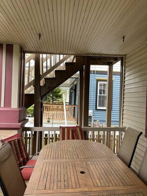 Eine überdachte Veranda mit einem Holztisch und -stühlen, einer Treppe und Blick auf ein blaues Haus.