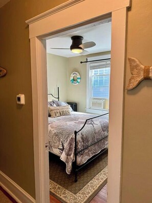 Ein Schlafzimmer mit einem Bett, einem Deckenventilator, einem Fenster mit Jalousien und einer Wanduhr.
