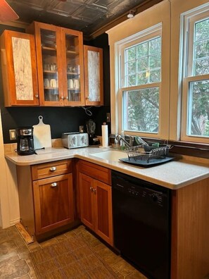 A kitchen with wooden cabinets, a dishwasher, a coffee maker, a toaster, and a window with a view of trees. - • Family Beach Condo • Walk to Beach • Porch (Ocean City)