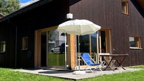 Moderni rakennus, jossa on suuri lasiovella varustettu sisäänkäynti, katettu ulkoalue pöytineen ja tuoleineen sekä nurmikkoalue.