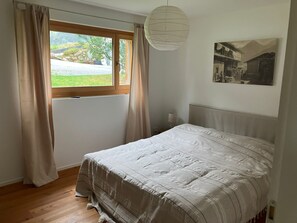 Ein Schlafzimmer mit Bett, einem Fenster mit Vorhängen, einer Wandleuchte und einem gerahmten Bild.