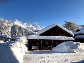 Eine Holzhütte mit schneebedecktem Dach, umgeben von verschneiten Bergen und Bäumen.