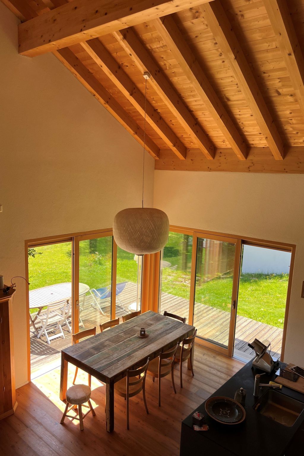 Ein Essbereich mit Holztisch und Stühlen, großen Fenstern und Blick ins Freie.