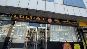 A modern building with a glass facade, a sign for 'Luluat Alkhaleej Hotel Apartments,' and a visible entrance with a glass door. - LuLuat Al Khaleej Hotel Apartments (AL KARAMA)