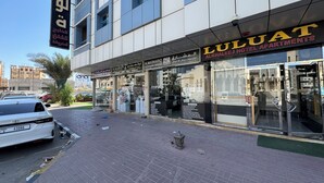 A hotel with a glass facade, a sign for Alkhaleej Hotel Apartments, and a visible entrance. - LuLuat Al Khaleej Hotel Apartments (AL KARAMA)