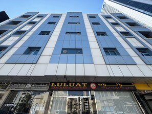 Un edificio moderno con varios pisos, que presenta un letrero llamativo para 'ALKHAALEJ HOTEL APARTMENTS' a nivel de calle.