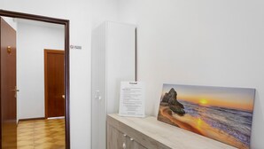 Un corridoio con pavimento in legno, una porta bianca e un armadietto con un quadro raffigurante un tramonto sull'oceano.