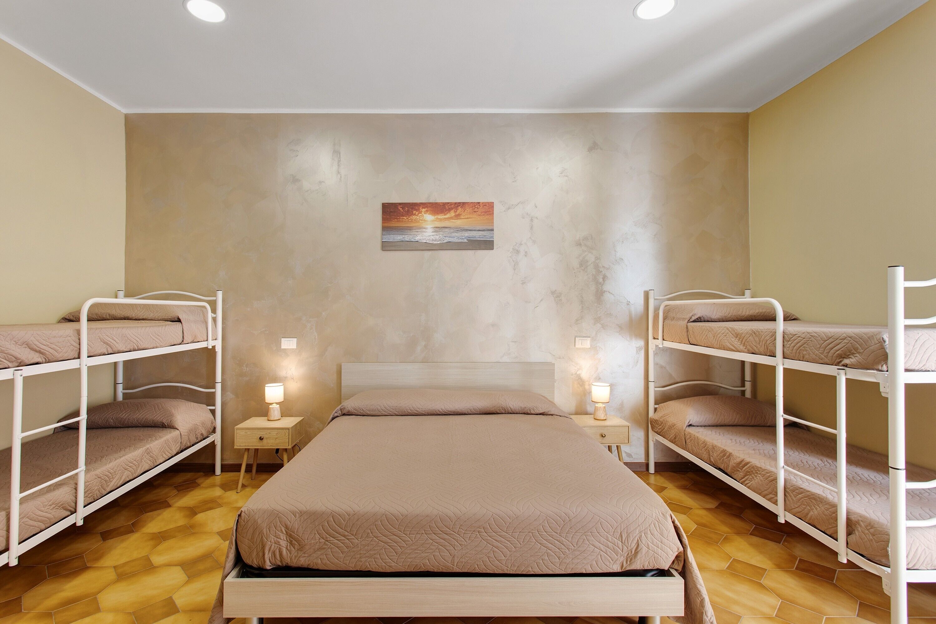 Une chambre avec des lits superposés, un lit simple, une table de chevet avec une lampe et un tableau au mur.