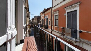 Una stretta via fiancheggiata da edifici, cielo sereno e un balcone con ringhiera.