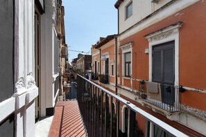 A narrow street with buildings on either side, a clear sky, and a balcony with a railing. - Dimora Sophia Nicole: In the Heart of Catania’s Charm (Catania)